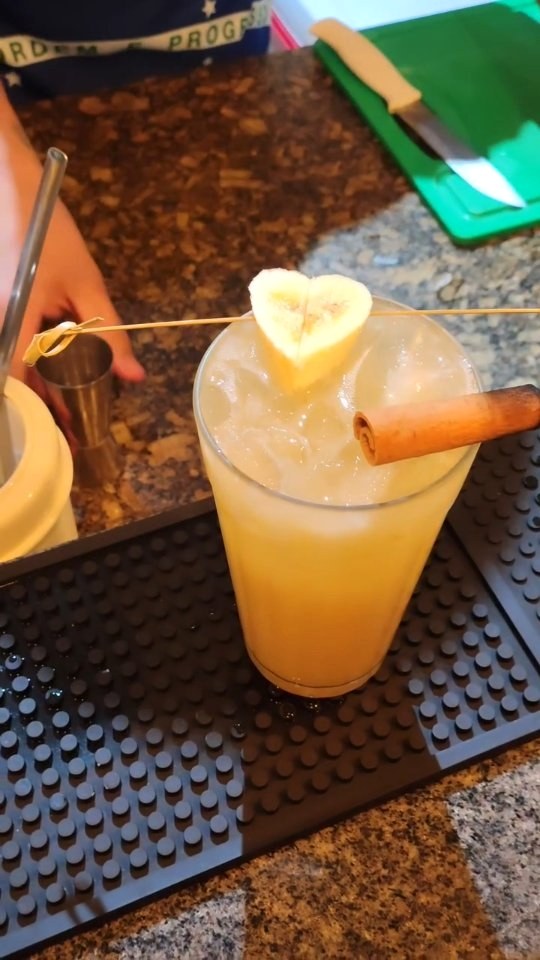 Bebida clara com gelo e guarnição, fotografada sobre uma bancada de bar.
