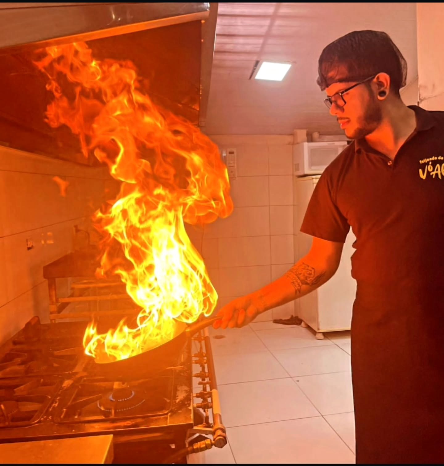 Julio Cabral trabalhando em uma cozinha enquanto uma chama se eleva de uma panela.