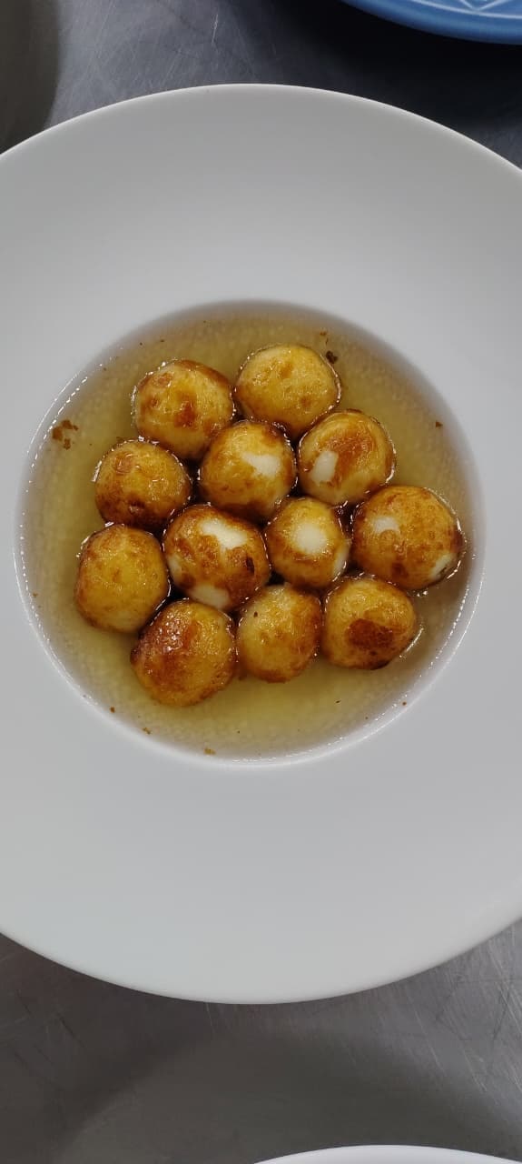 Pequenos preparos dourados servidos com molho em um prato branco.